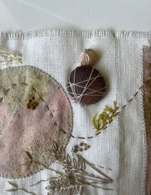 Textile art piece with embroidered elements and natural materials on a neutral background